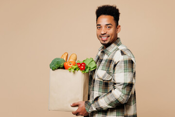 Side view young smiling happy man wear grey shirt hold paper bag for takeaway mock up with food products look camera isolated on plain pastel beige background Delivery service from shop or restaurant