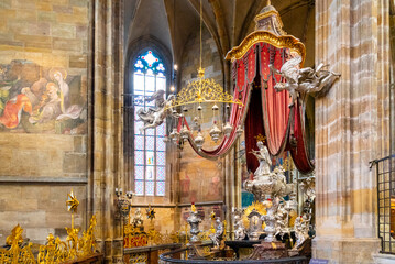 The ornate canopy of St. John of Nepomuk silver tomb, with its red drapery and intricate details, stands within the grand interior of Saint Vitus Cathedral. Prague, Czechia