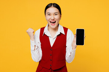 Young lawyer employee business woman of Asian ethnicity in red vest shirt work at office hold use blank screen mobile cell phone do winner gesture isolated on plain yellow background. Career concept