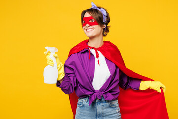 Young woman wears purple shirt rubber gloves super hero suit mask casual clothes do housework tidy up hold spray look aside isolated on plain yellow background studio portrait. Housekeeping concept.