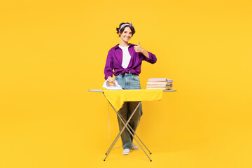 Full body young woman she wear purple shirt casual clothes do housework tidy up ironing clean clothes on board show thumb up isolated on plain yellow background studio portrait. Housekeeping concept. - obrazy, fototapety, plakaty