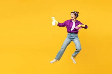 Fototapeta na wymiar Full body fun young woman wears purple shirt rubber gloves do housework tidy up hold in hand rag use spray bottle jump high isolated on plain yellow background studio portrait. Housekeeping concept.