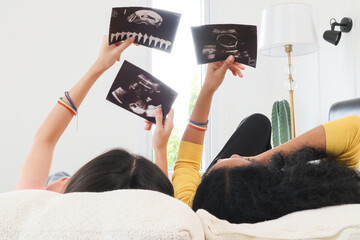 A multiracial lesbian couple lying watching ultrasound images, two lesbians feeling excited about...