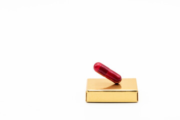Píldora de color rojo puesta en un lingote de oro de diferentes formas en equilibrio, aislado en blanco - obrazy, fototapety, plakaty