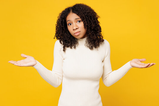 Little sad kid teen girl of African American ethnicity wear white casual clothes spread hand shrugging shoulders looking puzzled isolated on plain yellow background studio Childhood lifestyle concept