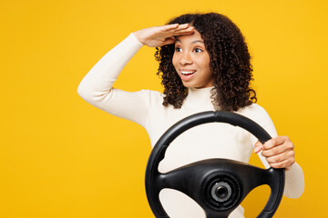 Fototapeta na wymiar Little fun kid teen girl of African American ethnicity wear white casual clothes hold steering wheel driving car look far away isolated on plain yellow background studio portrait. Lifestyle concept,