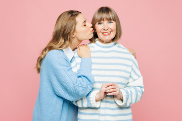 Elder smiling happy parent mom 50s years old with young adult daughter two women together wearing blue casual clothes hug kiss cheek isolated on plain pastel light pink background. Family day concept. - 769691456