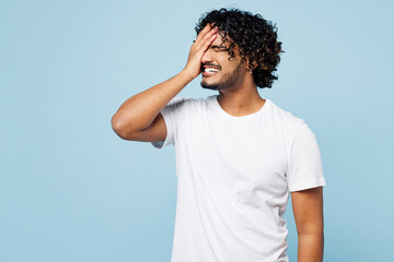 Young sad Indian man wear white t-shirt casual clothes put hand on face facepalm epic fail mistaken omg gesture isolated on plain pastel light blue cyan background studio portrait. Lifestyle concept.