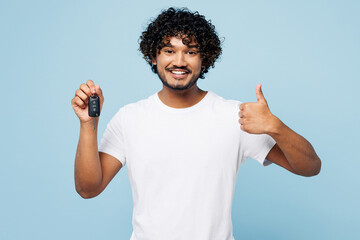 Young happy Indian man he wear white t-shirt casual clothes hold in hand car key fob keyless system show thumb up isolated on plain pastel light blue cyan background studio portrait Lifestyle concept