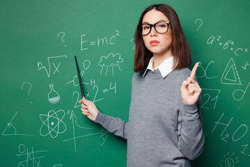 Young strict smart teacher woman wear grey casual shirt glasses hold pointer point finger up aware...