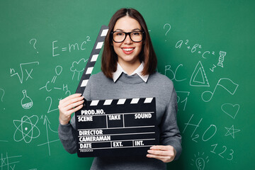 Young smart teacher woman in grey casual shirt glasses hold in hand classic black film making...