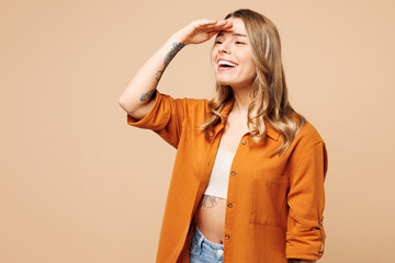 Side view young Caucasian woman she wears orange shirt casual clothes hold hand at forehead look far away distance isolated on plain pastel light beige background studio portrait. Lifestyle concept. - obrazy, fototapety, plakaty