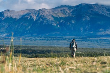 Fly fisherman walking in the grassy field on the background of mountains