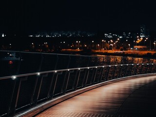 an illuminated bridge over the water with lights on in the distance