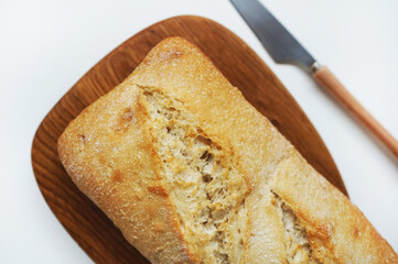 Wheat ciabatta on a board next to a knife on a white background