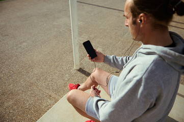 Overhead view sportsman wearing earphones, using smartphone with blank black mockup digital touch screen after workout