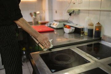 Kitchen worker meticulously cleans countertop surface with soft clothes. Responsible employee...