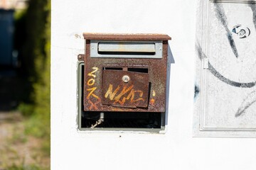 Old, rusty, metal mailbox attached to a white wall