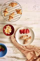 Breakfast set with freshly-baked croissants, and a handful of ripe strawberries on a table