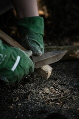 Man in protective gloves carefully carves a piece of wood using a knife with a blurry background