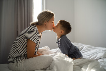 Happy mother and her little son relaxing in bed in morning hours