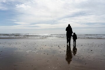 Naklejka premium Man walking their child along a sun-drenched sandy beach