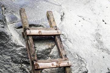 An old and rotten wooden ladder was propped up against a boulder. Wood ladder on solid stone wall...