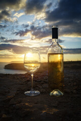 Bottle and glass of white wine against a breathtaking seaside sunset