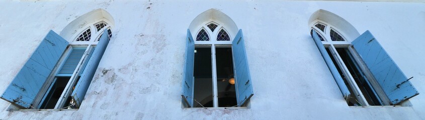 Three open windows with blue shutters of a church.