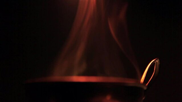 Closeup video of a person adding spices to hot pot on a black background