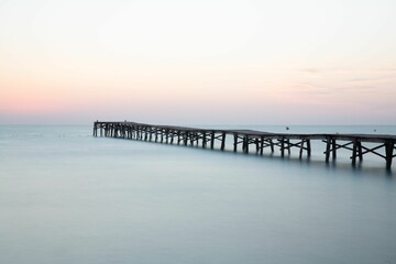 a wooden pier in the water at sunset with birds flying