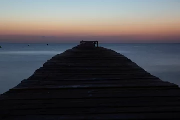Fotobehang the end of a pier next to the ocean in front of a sunset © Wirestock