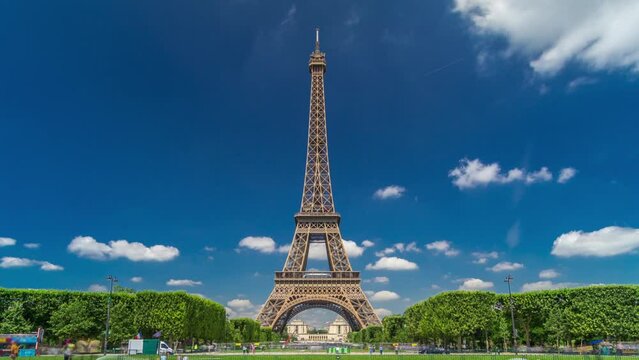 Eiffel Tower on Champs de Mars in Paris timelapse hyperlapse, France. Blue cloudy sky at summer day with green lawn and fountain with traffic around