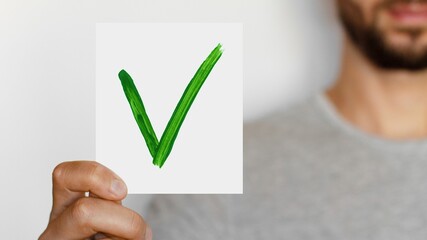 Close-up of a man holding a piece of paper with a green check mark on it