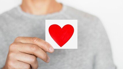 Close-up of a man holding a piece of paper with a red heart on it