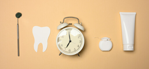 Fototapeta na wymiar Alarm clock, tube of toothpaste and paper tooth on brown background, oral hygiene care