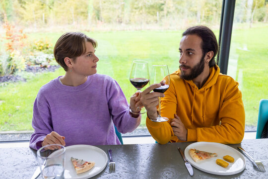 This inviting photograph captures two friends sharing a moment over wine, exchanging meaningful glances that suggest deep conversation and understanding. The casual dining experience with pizza slices