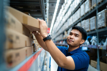 A man in a blue shirt is reaching for a box on a shelf in a warehouse. Concept of hard work and...