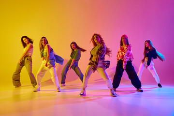 Group of stylish young women dancing contemp, hip hop dance in casual clothes against gradient background in neon light. Concept of youth, street dance, contemporary dance, modern, dynamics