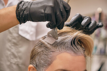 The hairdresser dyes the hair of the client. Tinting hair in a salon. Shallow depth of field