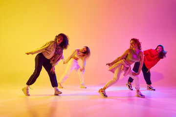 Beautiful young women, dancers in motion in casual clothes dancing against gradient background in neon light. Concept of youth, street dance, contemporary dance, modern, dynamics