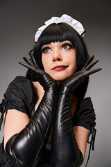 good looking young cosplayer in maid costume posing alluringly and looking away on gray backdrop