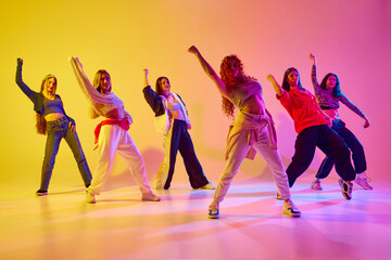 Young talented, beautiful women dancing hip hop, contemp, freestyle against gradient background in neon light. Concept of youth, street dance, contemporary dance, modern, dynamics