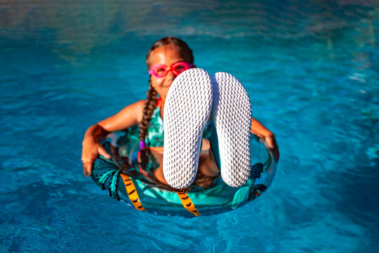 A teenager girl relaxes on a pool ring, her sneaker soles upturned towards the camera, ready for an overlay of text. Leisure, youth, and fun in the sun. - Powered by Adobe
