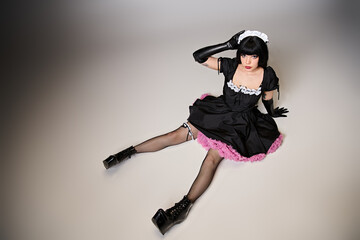 glamorous sexy female cosplayer in tempting maid costume looking at camera on gray background