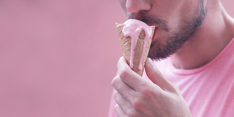 Pink color obsession concept. Close-up fashion portrait of young man eating melting ice cream over magenta background. Copy-space. Outdoor shot