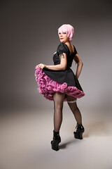 sexy stylish woman in black dress with pink hair cosplaying anime character and looking at camera