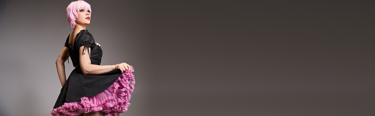 appealing woman cosplaying anime character with pink hair and looking away on gray backdrop, banner