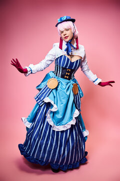 alluring modish female cosplayer in blue hat and vivid dress looking at camera on pink backdrop