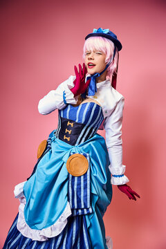 tempting sexy female cosplayer in blue hat and vibrant attire looking at camera on pink backdrop